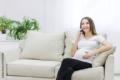 Pregnant woman talking over the phone on white sofa.