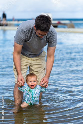 Happy baby walking through sea water in ocean pool at first trip to the beach photo