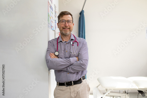 Male doctor with stethoscope around his neck standing while leaning on the wall in the clinic photo