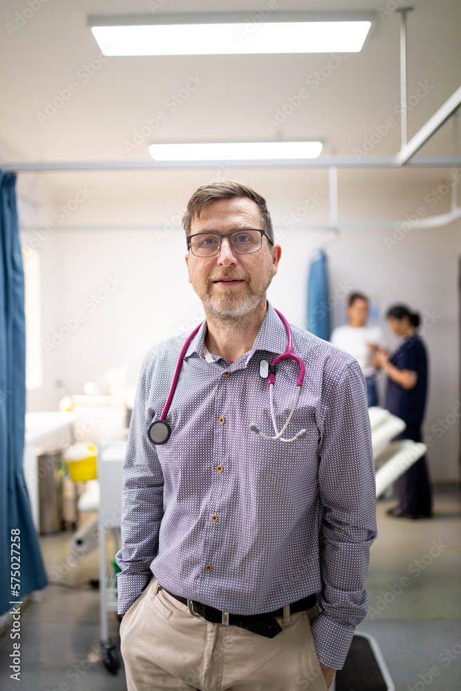 Smiling middle-aged male doctor with a stethoscope around his neck standing in the clinic Smiling middle-aged male doctor with a stethoscope around his neck standing in the clinic