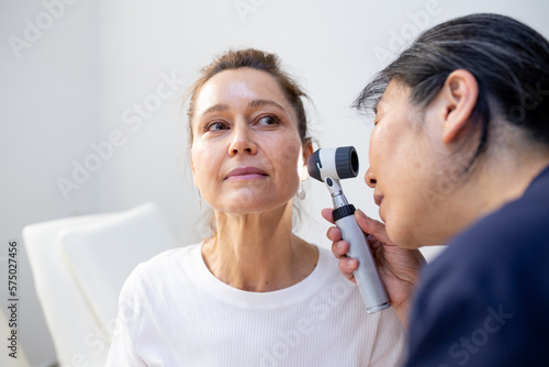 Female patient having her ears checked by a female nurse using an otoscope in the clinic
