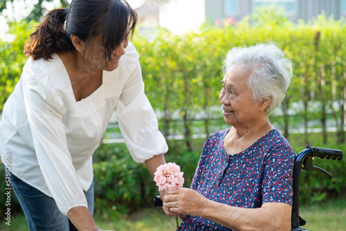 Caregive talk and help Asian elderly woman holding flower, smile and happy in the sunny garden. © amazing studio