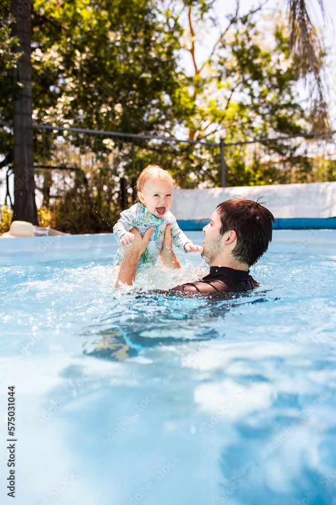Father playing with baby in swimming pool dad lifting child high into air splashing in water Father playing with baby in swimming pool dad lifting child high into air splashing in water