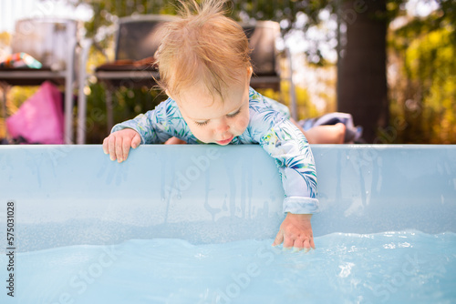 Young baby leaning over edge of inground swimming pool splashing in water – dangerous situation photo