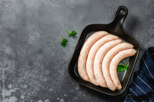 Raw turkey sausages on dark ceramic dish, cast iron skillet, dark background. Top view, copy space.
