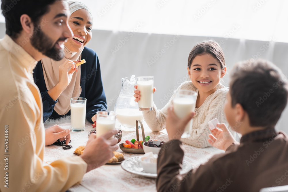 Positive muslim family holding glasses of milk and talking near food during suhur at home. Positive muslim family holding glasses of milk and talking near food during suhur at home.