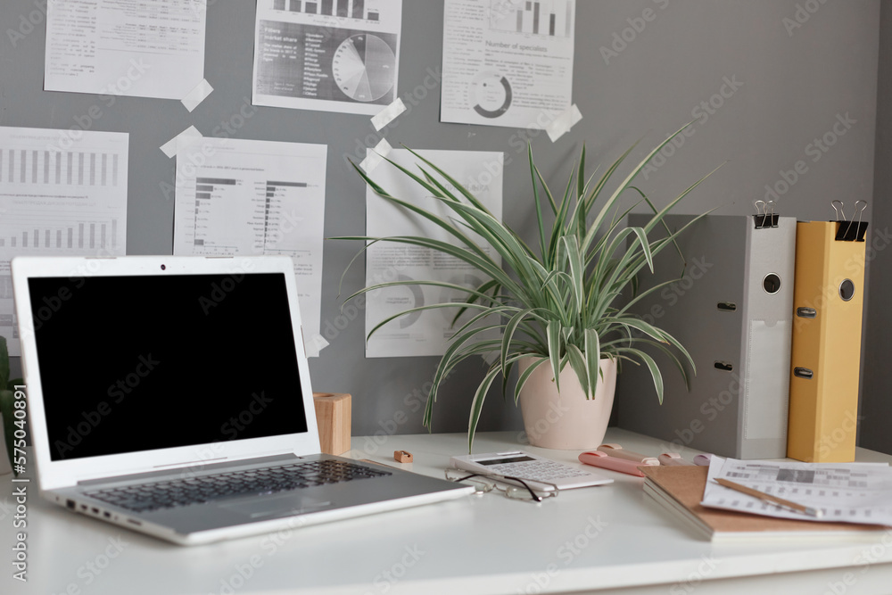Fototapeta premium Workplace at home or in office with table, laptop with empty display, flower, paper folders, notes on wall.