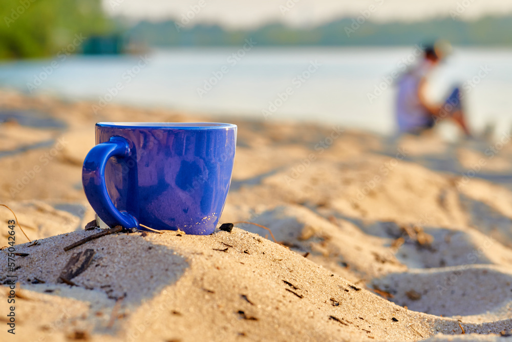 Blue ceramic cups for coffee tea beverages on the sand beach shore of a river Blue ceramic cups for coffee tea beverages on the sand beach shore of a river