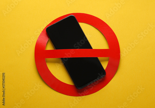 Smartphone with red prohibition sign on yellow background. Ban photo