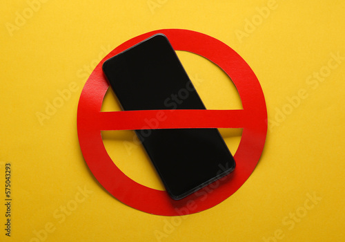 Foto Smartphone with red prohibition sign on yellow background. Ban