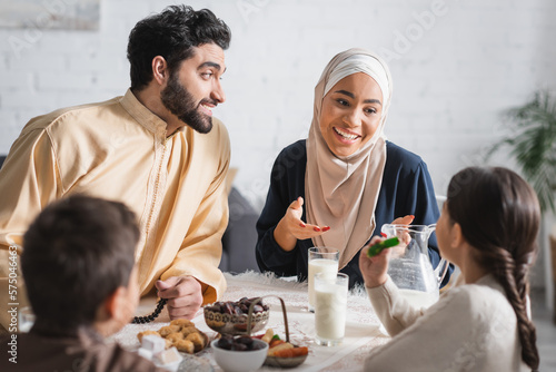 Positive muslim family talking to kids during suhur breakfast at home.