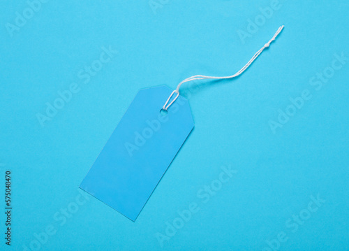 Blue blank clothing price tag or label mockup with string on blue background. Sale, shopping concept. Top view