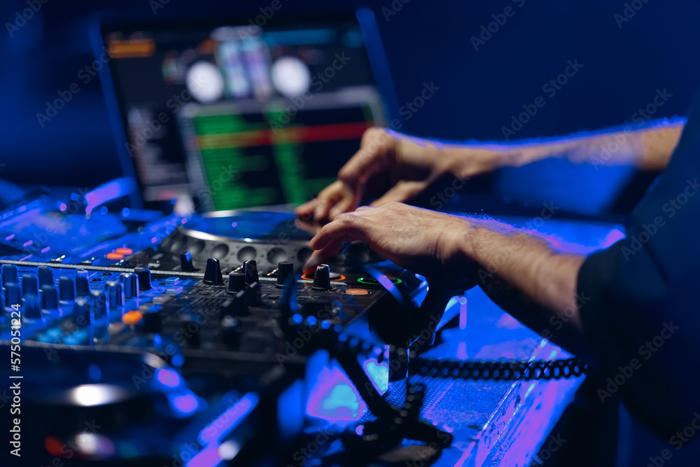 Hands of DJ playing music on rave party in night club. Professional disc jockey mixing musical tracks on stage