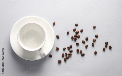 Ceramic coffee cup with coffee beans on gray background. Top view