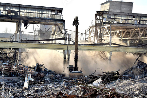 A powerful excavator breaks the reinforced concrete pillars of the plant