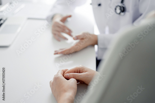 Doctor and patient discussing current health examination while sitting at the desk in clinic office. The focus is on female patient's hands, close up. Medicine concept.