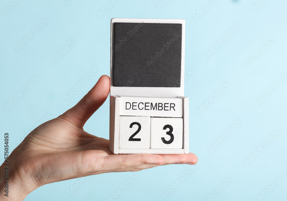 Female hand holding wooden calendar with date december 23 isolated on blue background Female hand holding wooden calendar with date december 23 isolated on blue background