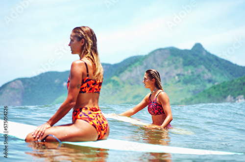 two young caucasian women sitting on surfboard in the ocean waiting for a wave to surf in Brazil