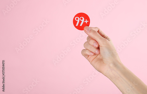 Hand holding paper cut notification with number 99 on pink background. Social media, message, sms, subscribe notice alert and reminder.