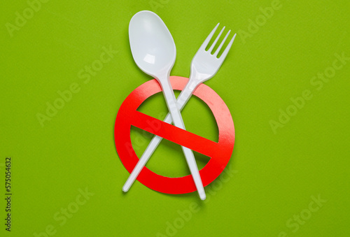 Plastic fork with a spoon with red prohibition sign on a green background. Plastic free, eco friendly concept. Top view. Flat lay