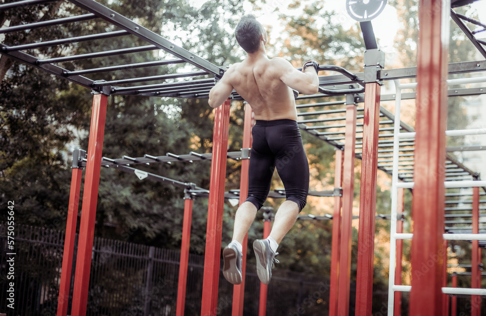Athletic male athlete with a naked torso pulls himself up on the workout ground. Outdoor workout