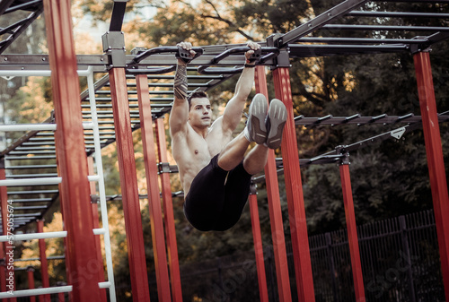 Athletic male athlete with a naked torso trains the abdominal muscles by lifting his legs up on workout ground. Outdoor workout