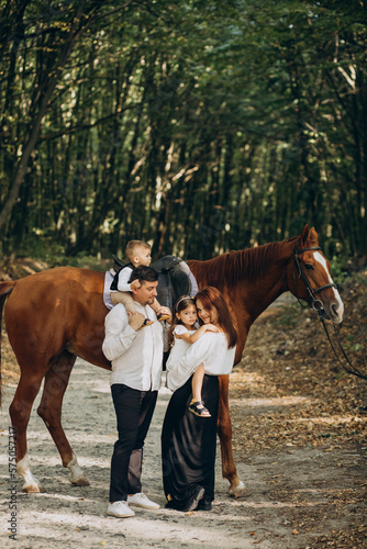 Young family with kids having fun with horse in forest