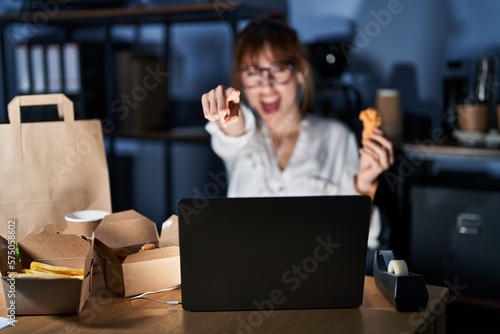 Young beautiful woman working using computer laptop and eating delivery food pointing displeased and frustrated to the camera  angry and furious with you