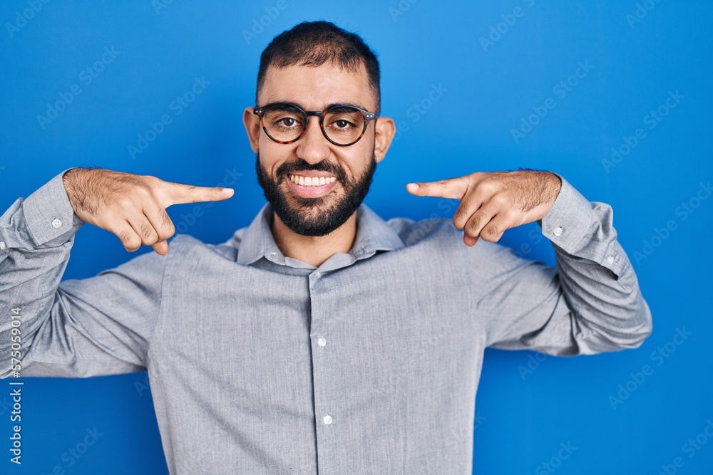 Naklejka premium Middle east man with beard standing over blue background smiling cheerful showing and pointing with fingers teeth and mouth. dental health concept.