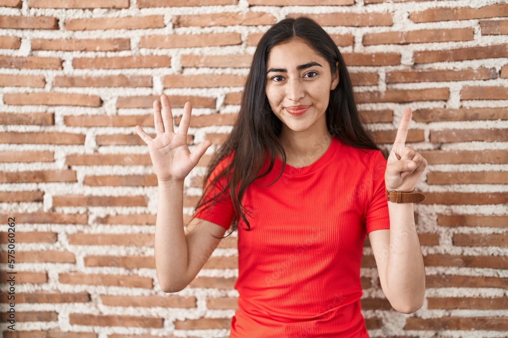 Young teenager girl standing over bricks wall showing and pointing up with fingers number six while smiling confident and happy. Young teenager girl standing over bricks wall showing and pointing up with fingers number six while smiling confident and happy.