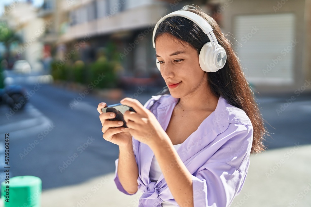 Young beautiful hispanic woman playing video game with serious expression at street
