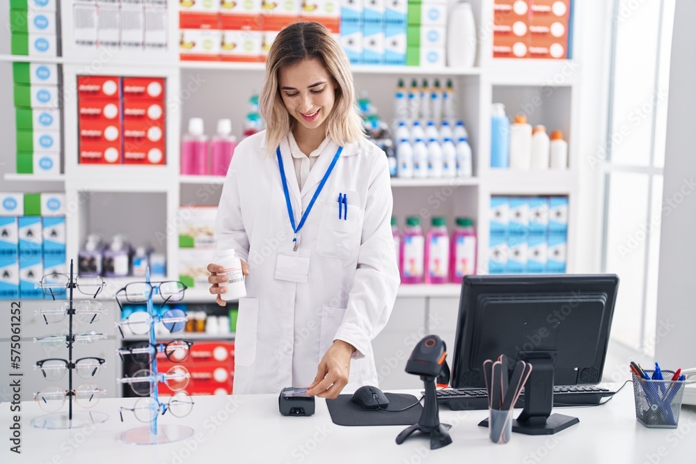 Young woman pharmacist charging pills bottle using credit card at pharmacy