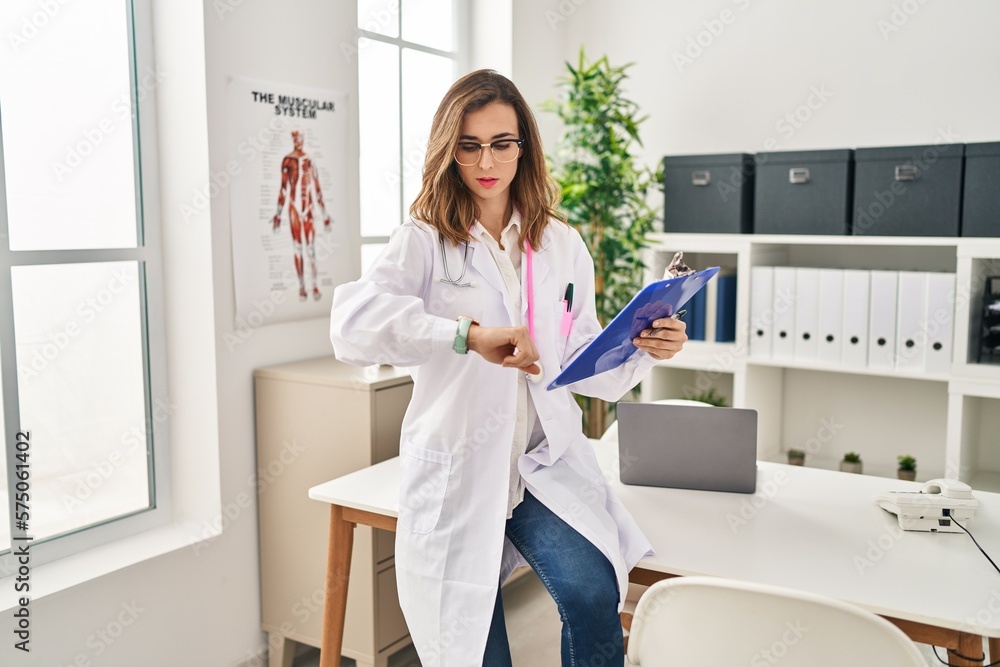Young woman wearing doctor uniform looking watch at clinic