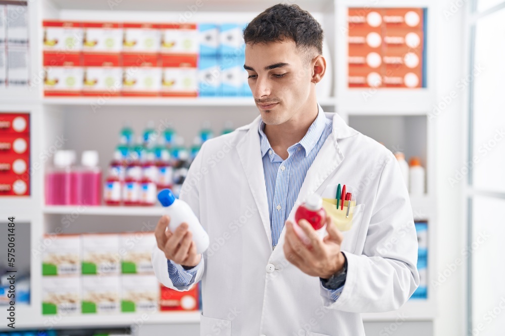 Young hispanic man pharmacist smiling confident holding medication bottles at pharmacy