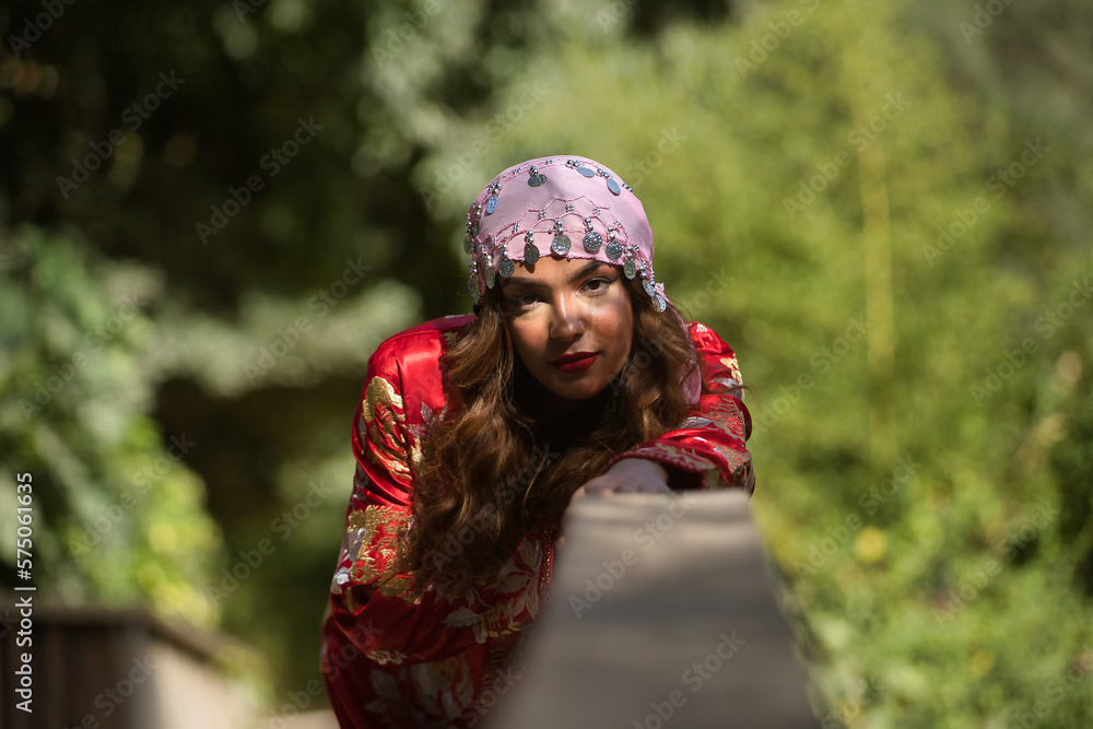 Beautiful young woman in a typical Moroccan red suit, embroidered with gold and silver threads, with a scarf with coins on her head, leaning on a wooden railing. Concept ethnicity, Marrakech, Arab. Beautiful young woman in a typical Moroccan red suit, embroidered with gold and silver threads, with a scarf with coins on her head, leaning on a wooden railing. Concept ethnicity, Marrakech, Arab.