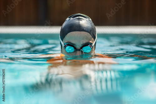 close up of female swimmer in swimming cap and goggles in swimming pool, water surface angle © Sergey Chumakov