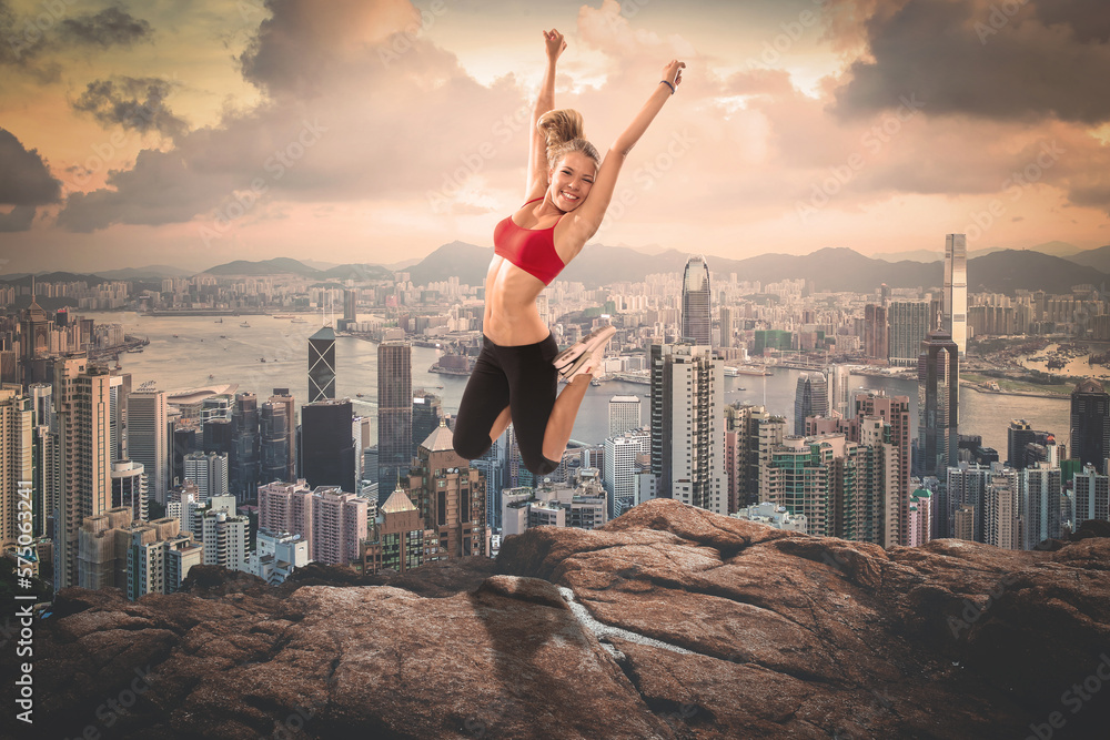 A blond girl jumping up on rocks in front of a cityscape
