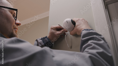 Installer in uniform puts security camera on wall fastening and connects it to system with cable. Man installs cameras in house. Concept of CCTV cameras  monitoring  safety and privacy.