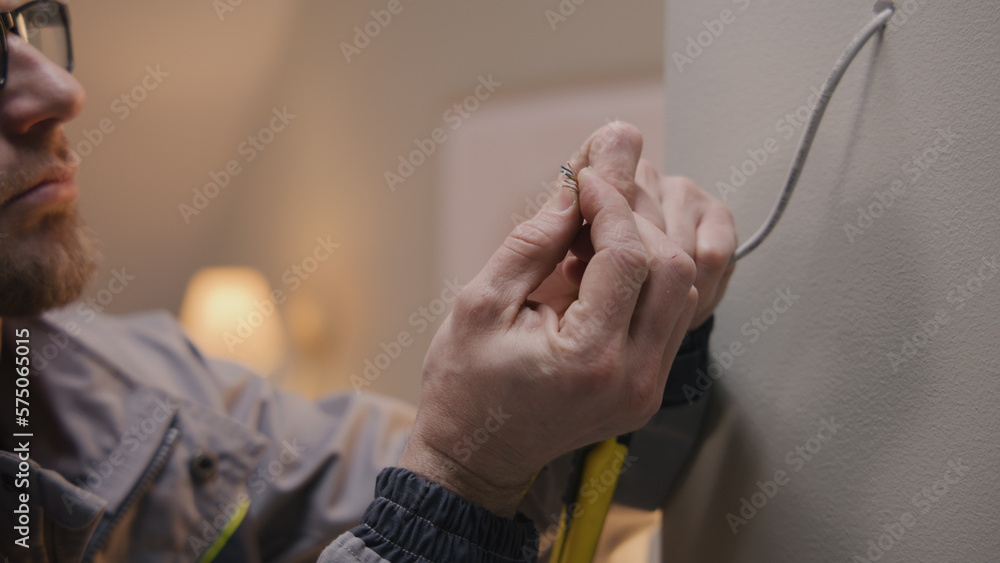 Close up shot of repairman in uniform and glasses works with cable twisted pair. Electrician removes insulation from wire with professional tool in the apartment. Installation of the Internet.