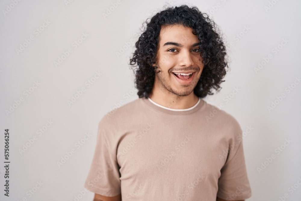 Hispanic man with curly hair standing over white background smiling cheerful with open arms as friendly welcome, positive and confident greetings Hispanic man with curly hair standing over white background smiling cheerful with open arms as friendly welcome, positive and confident greetings