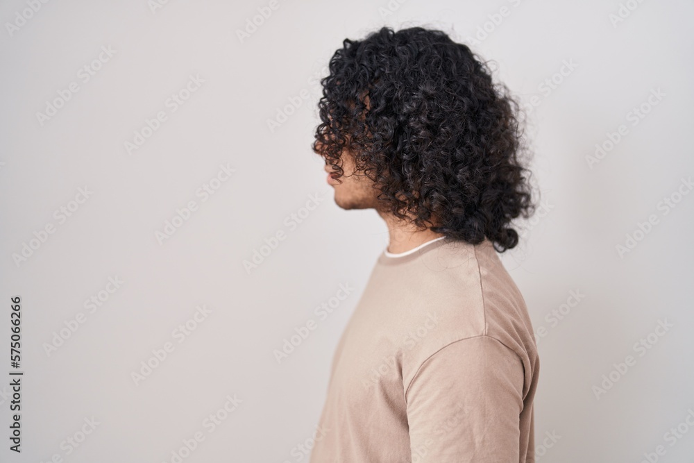 Hispanic man with curly hair standing over white background looking to side, relax profile pose with natural face and confident smile. Hispanic man with curly hair standing over white background looking to side, relax profile pose with natural face and confident smile.