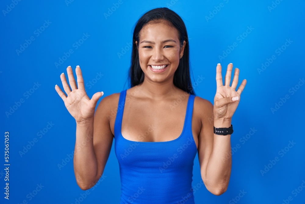 Fototapeta premium Hispanic woman standing over blue background showing and pointing up with fingers number nine while smiling confident and happy.