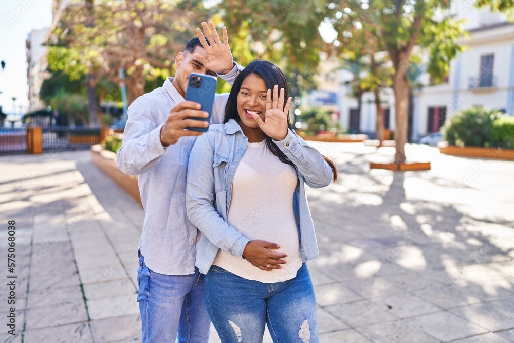 Young latin couple expecting baby having video call at park