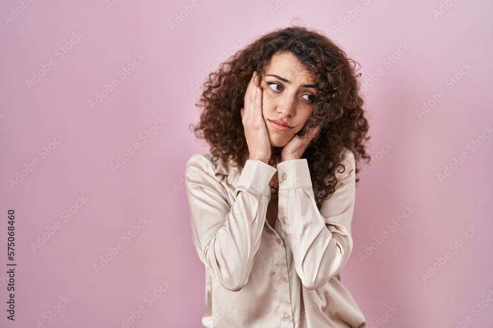 Hispanic woman with curly hair standing over pink background tired hands covering face, depression and sadness, upset and irritated for problem