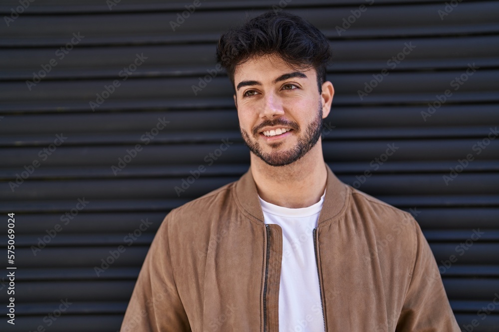 Young hispanic man smiling confident looking to the side over black isolated background Young hispanic man smiling confident looking to the side over black isolated background