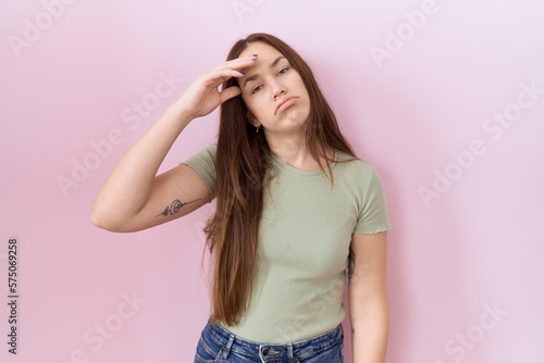 Beautiful brunette woman standing over pink background worried and stressed about a problem with hand on forehead, nervous and anxious for crisis