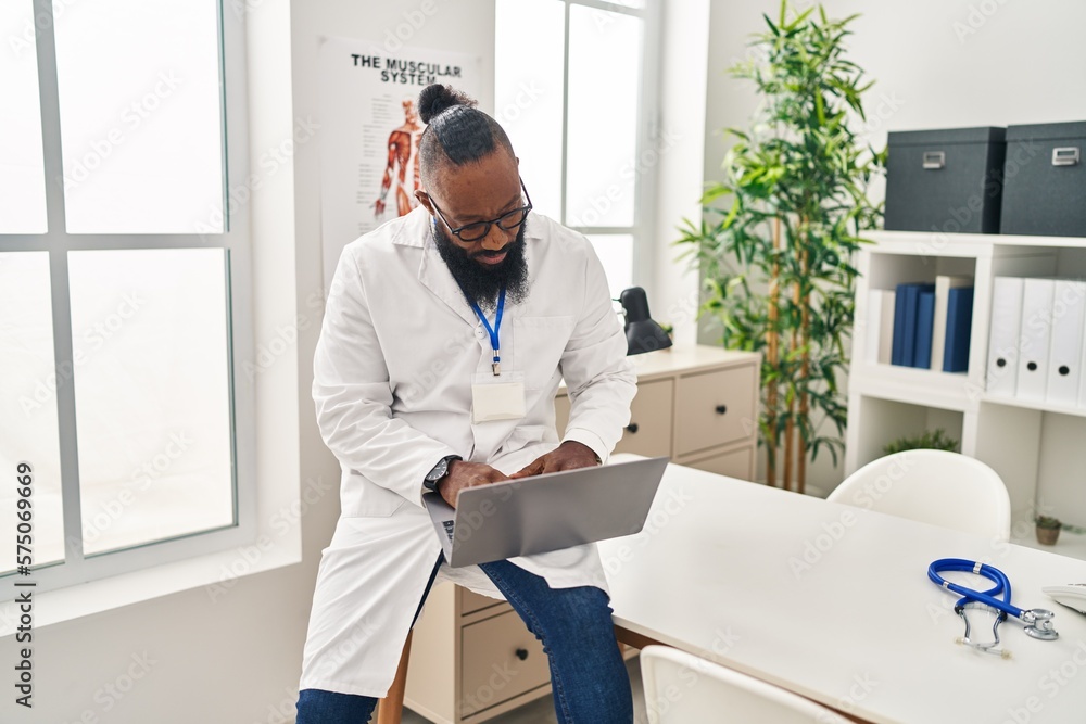 Young african american man wearing doctor uniform using laptop at clinic