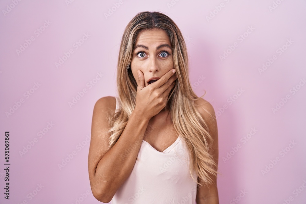 Young blonde woman standing over pink background looking fascinated with disbelief, surprise and amazed expression with hands on chin Young blonde woman standing over pink background looking fascinated with disbelief, surprise and amazed expression with hands on chin