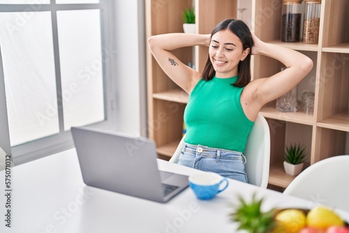 Young hispanic woman using laptop sitting on table at home