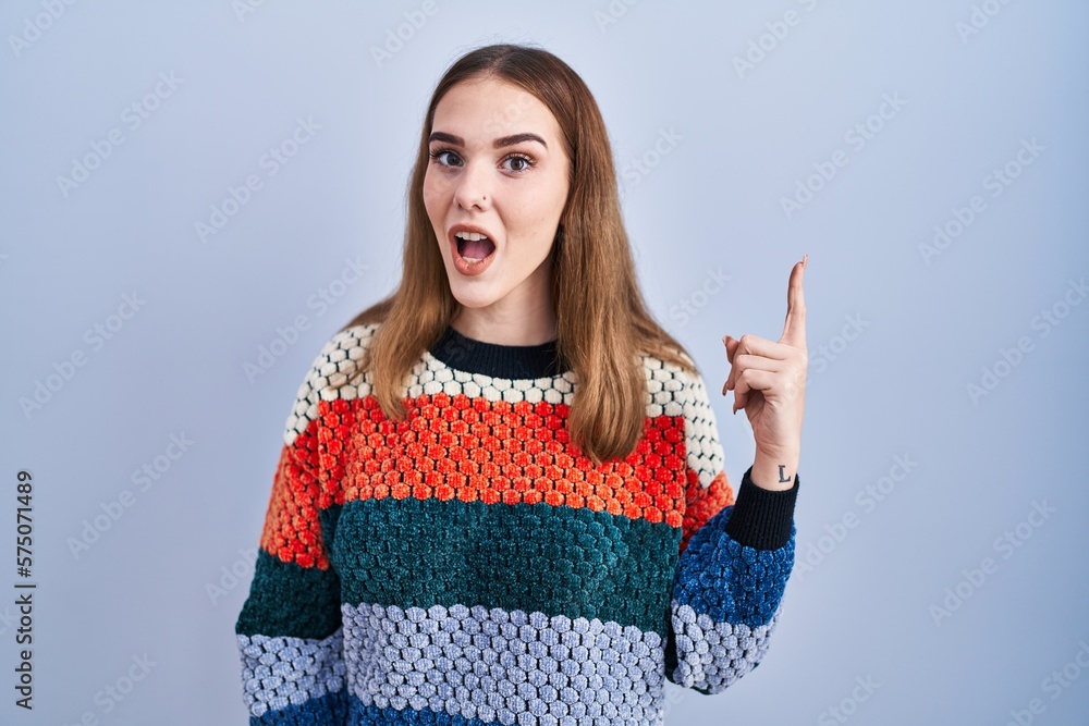 Young hispanic girl standing over blue background pointing finger up with successful idea. exited and happy. number one. Young hispanic girl standing over blue background pointing finger up with successful idea. exited and happy. number one.